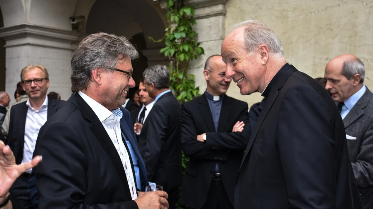 Kardinal Christoph Schönborn spricht bei einem Empfang mit ORF-Generaldirektor Alexander Wrabetz. Im Hintergrund stehen weitere Gäste im Innenhof eines historischen Gebäudes.