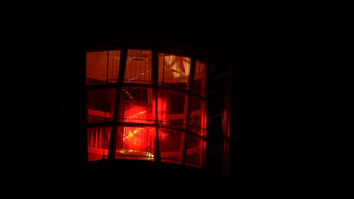 Rotes Nachtfeuer in einem Leuchtturm. Die Signalbeleuchtung ist hinter den Glasscheiben der Laterne vor dem dunklen Nachthimmel sichtbar.