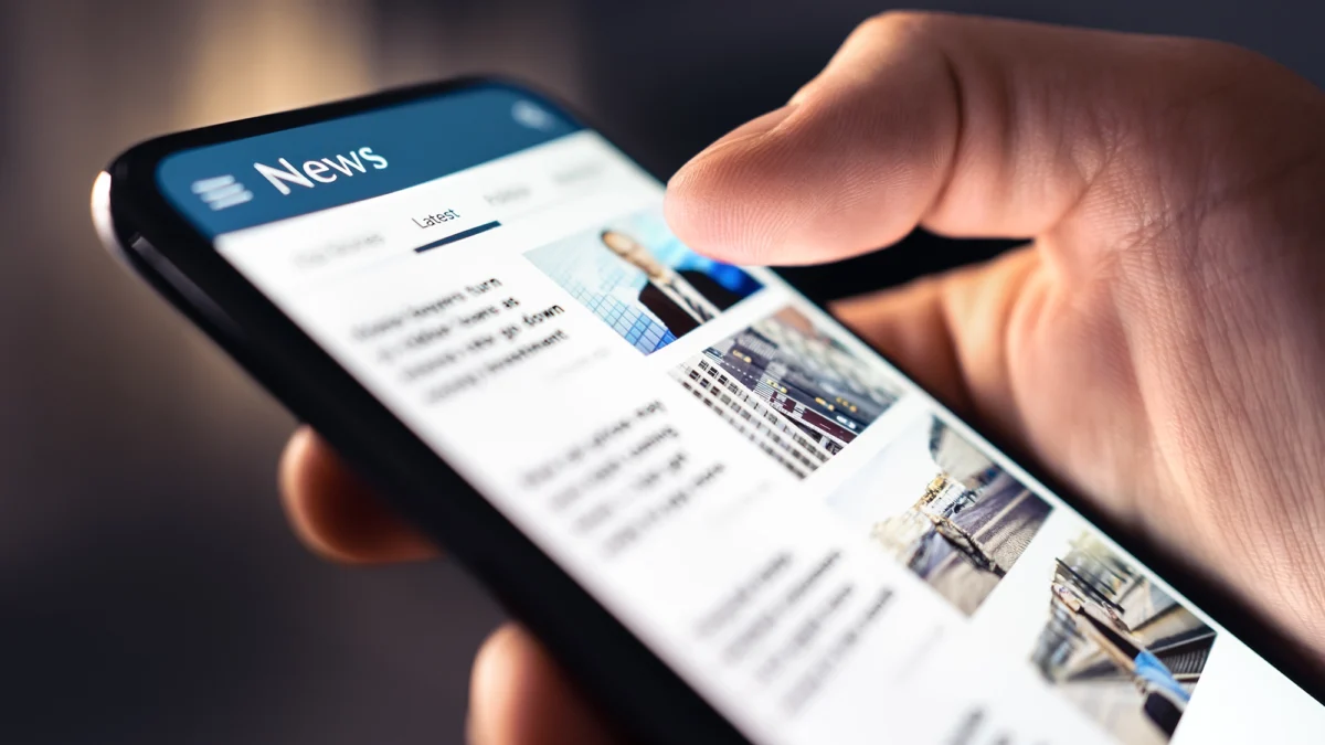Nahaufnahme einer Hand, die auf einem Smartphone durch eine Nachrichten-App mit aktuellen Meldungen scrollt.