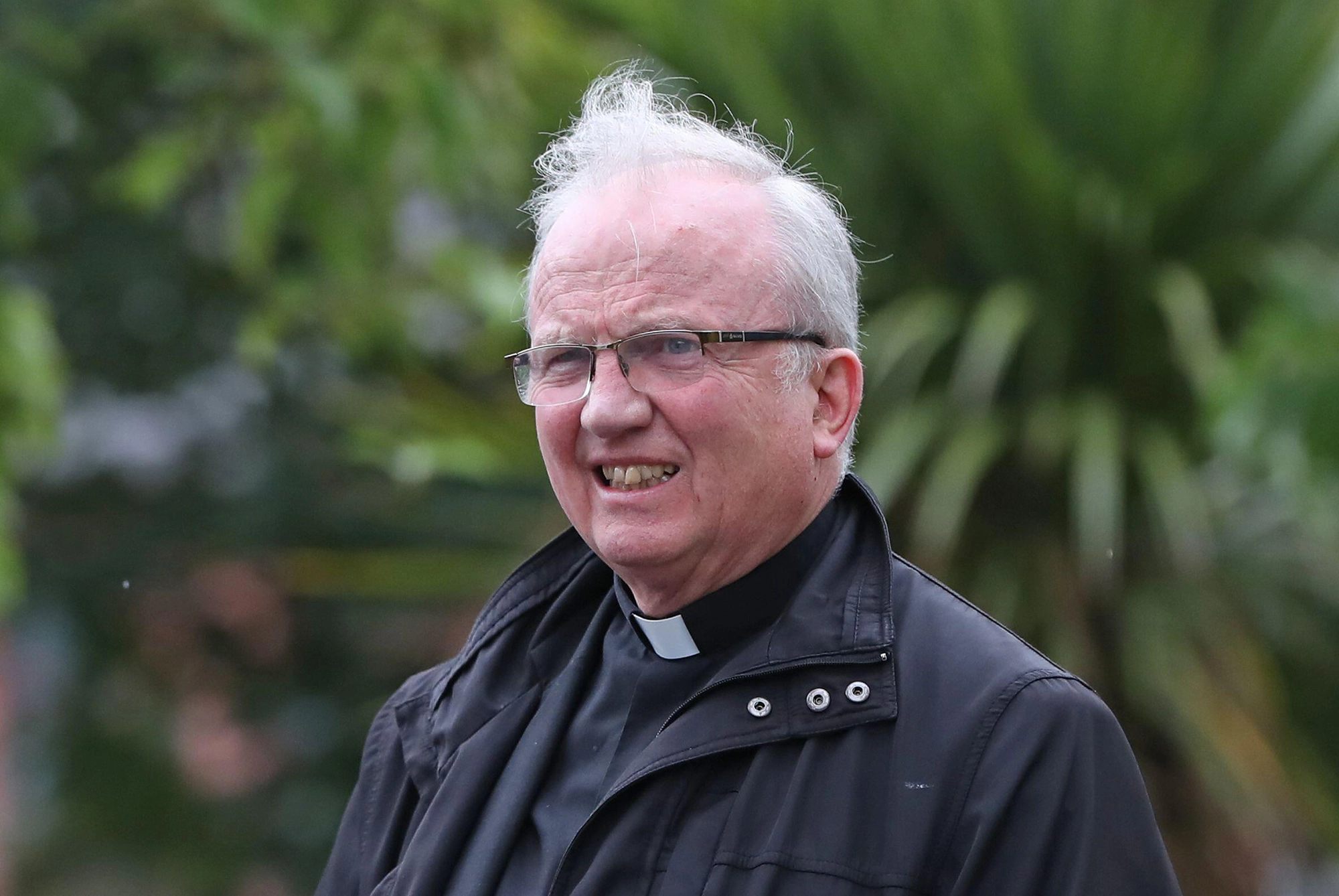 Interview mit Bischof Donal McKeown 1 Mann mit Brille und grauen Haaren trägt eine schwarze Jacke und einen Priesterkragen, steht im Freien vor grünem, verschwommenem Hintergrund.