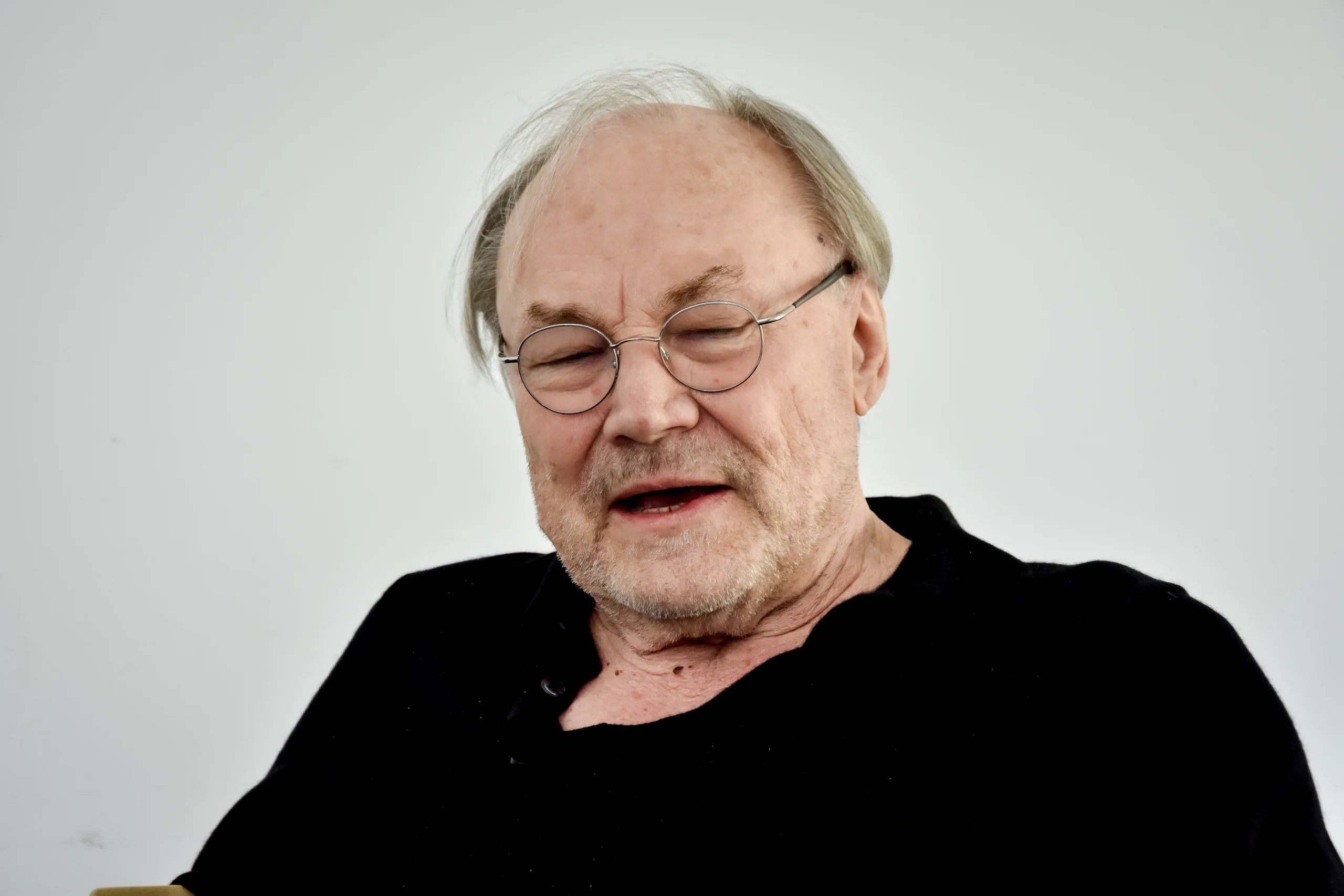 Klaus Maria Brandauer mit geschlossenen Augen während des Interviews, in schwarzem Pullover und Brille.