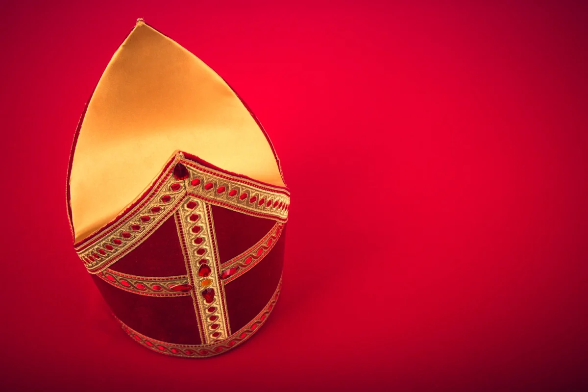 Rotgoldene Mitra, traditionelle Bischofsmütze, vor rotem Hintergrund.