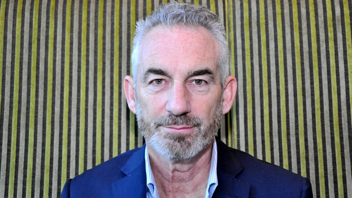 Portrait of economist Tim Jackson in a blue jacket, sitting in front of a vertically striped background